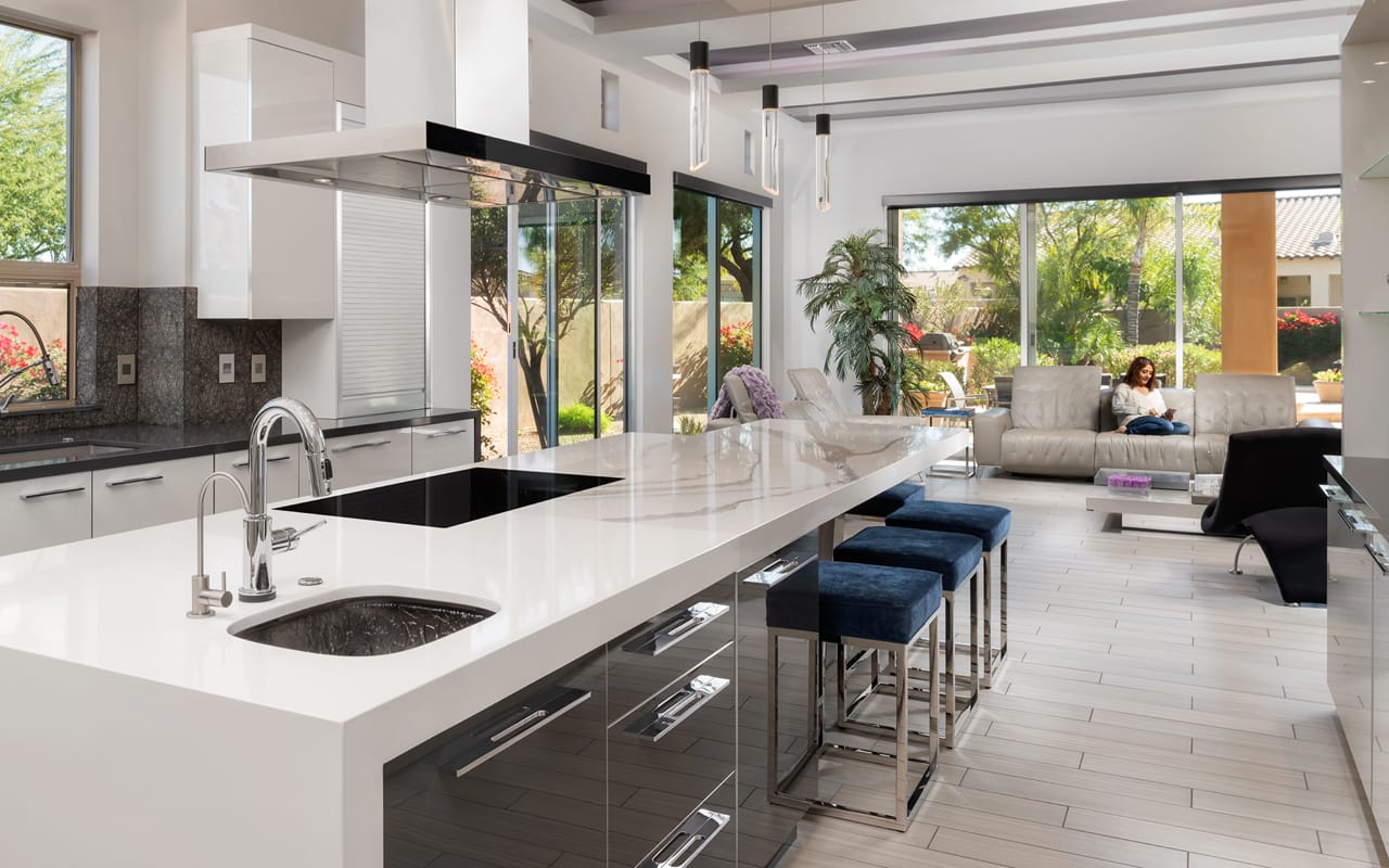 White and grey Contemporary kitchen with a woman reading a book on a couch in the background.