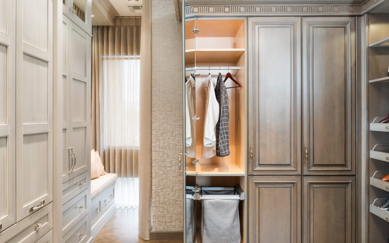Closet with cream and wood grain cabinetry. One of the closet doors is open revealing a hamper and hanging clothes.