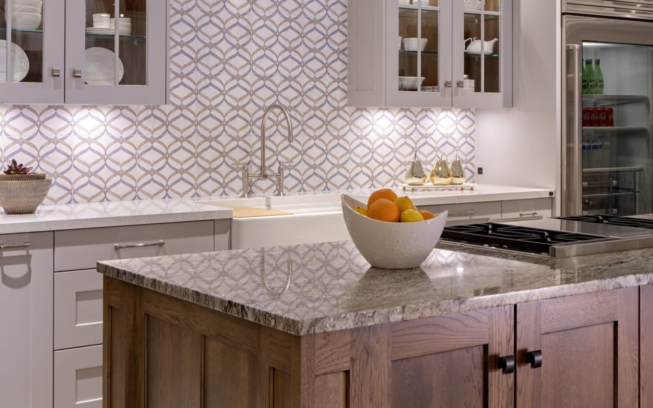 Transitional style kitchen with beige shaker-style cabinets. The upper cabinets have glass inserts. There is a farmhouse sink and a range cooktop on the warm-toned woodgrain island.